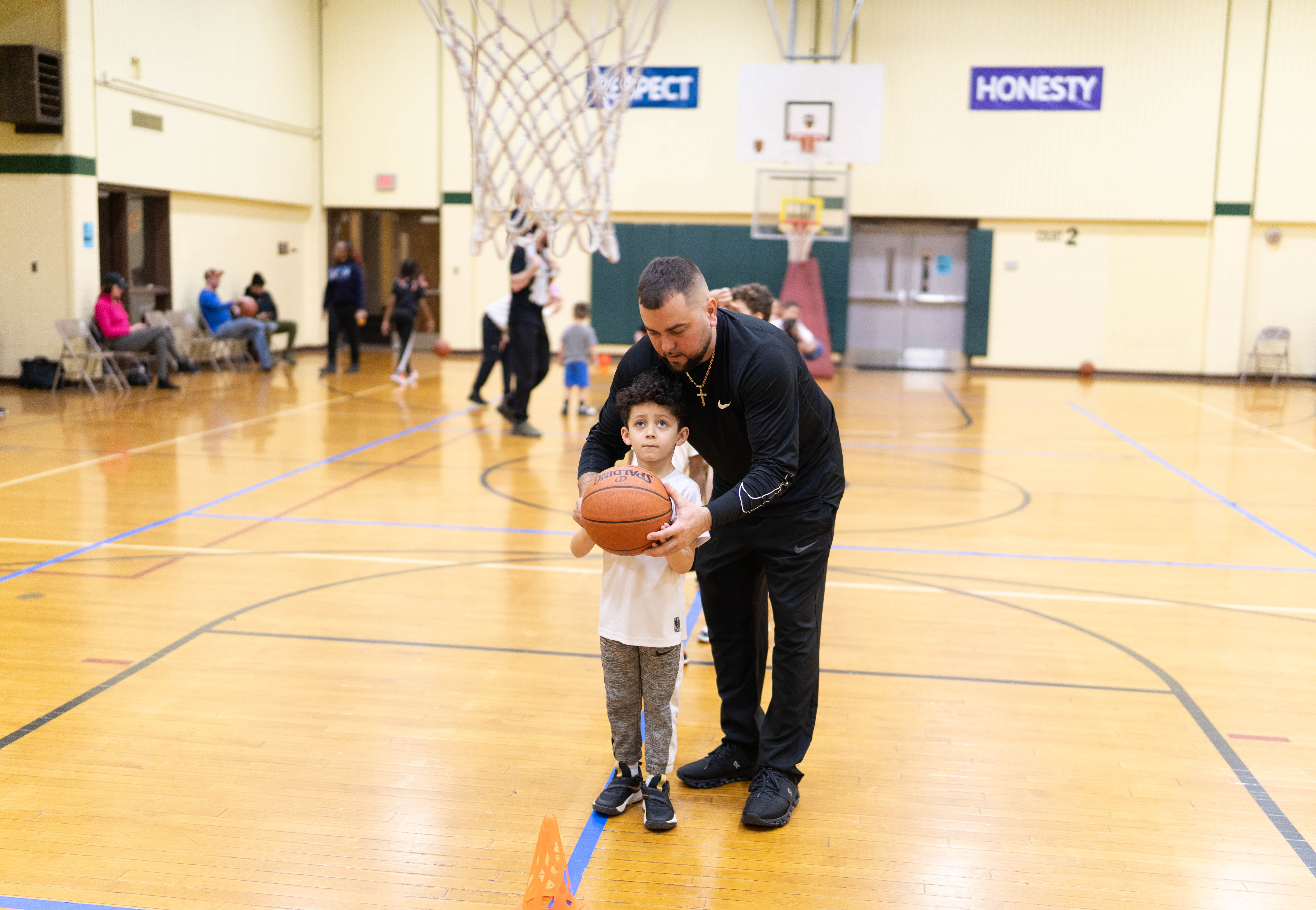 A YMCA coach helping a young child learn to hold and shoot a basketball