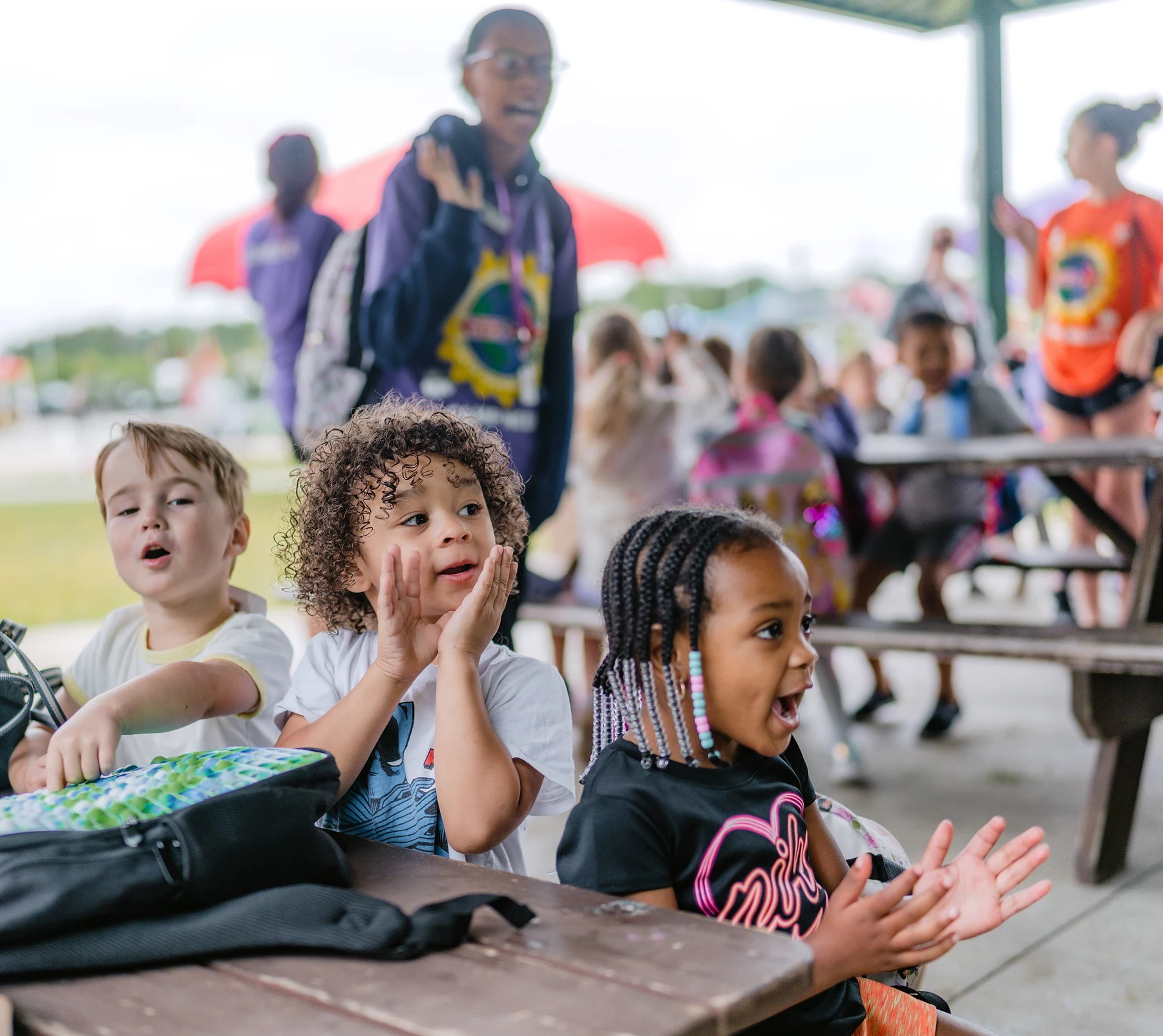 Camp Curiosity children reacting with excitement at an outdoor picnic table
