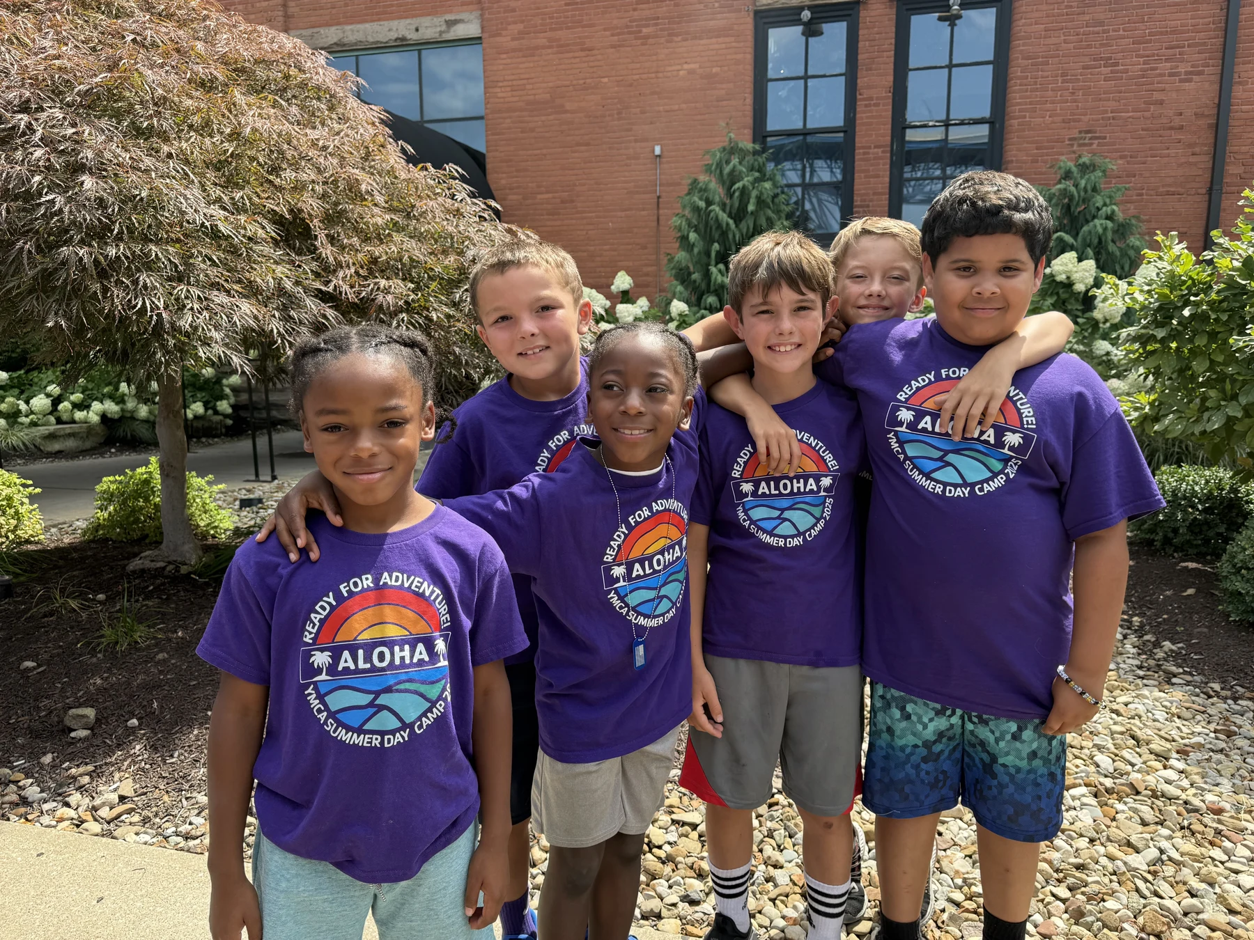 Six Davis day campers smiling together outdoors in purple camp shirts